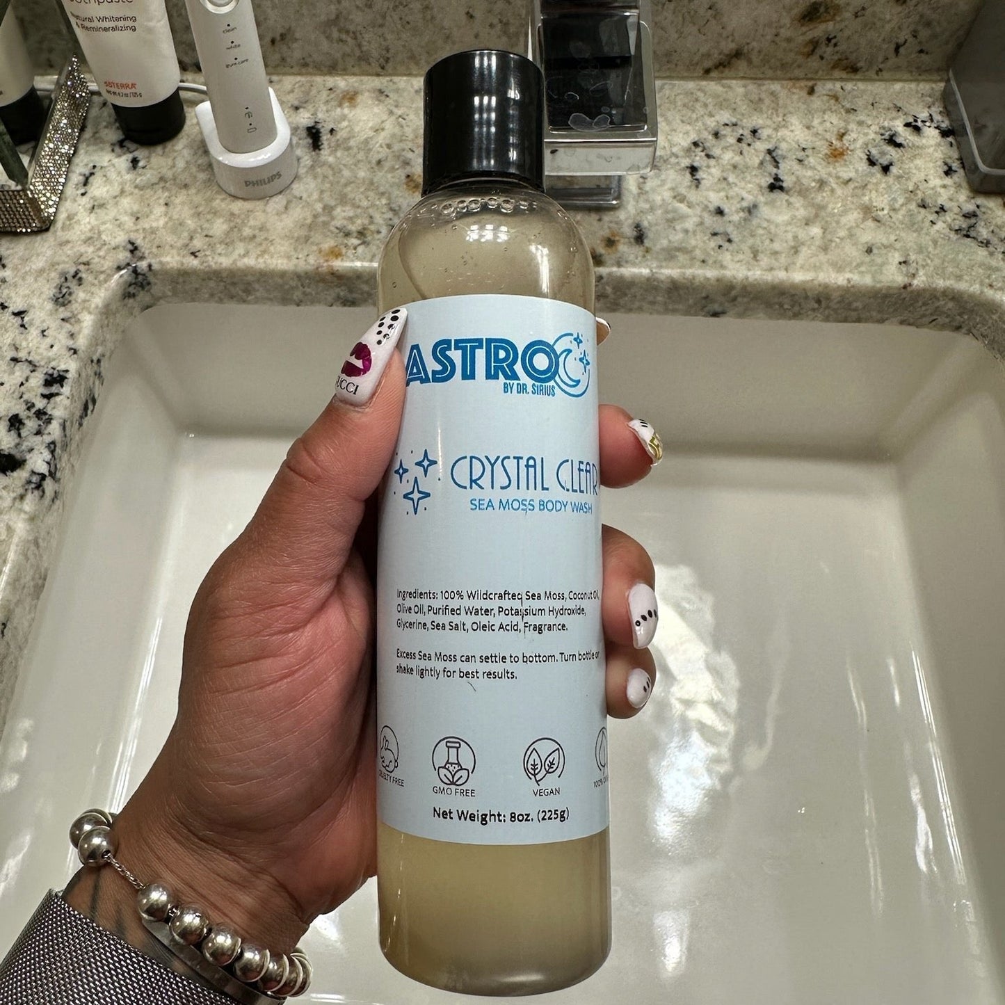 Astro Body Wash Crystal Clear Sea Moss hydrating vegan body wash bottle held over bathroom sink granite countertop